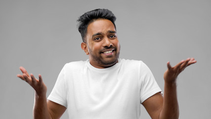 people, emotion and expression concept - confused indian man shrugging over grey background