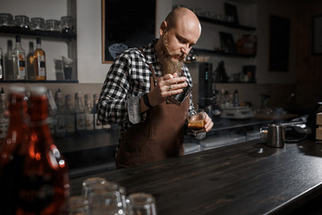 Brutal young barista in an apron makes coffee at the bar in a modern cafe