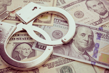 Pair of metal police handcuffs on USD US dollar banknotes money cash background.  Corruption, dirty...