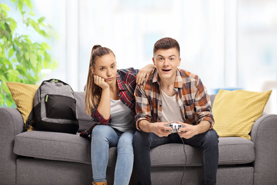 Bored teenage girl sitting next to a boy playing video games on a sofa