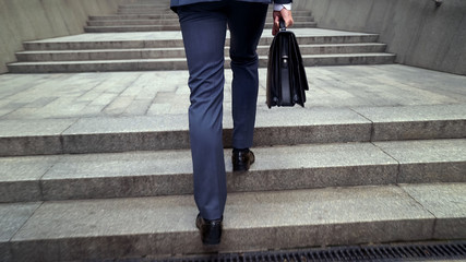 Male in suit holding leather briefcase climbing stairs to office building career