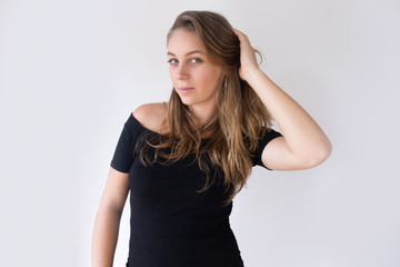 Pretty Caucasian girl holding hand behind head and brushing hair with fingers. Young woman in black dress checking her appearance. Mirror concept