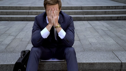 Desperate male sitting on ladder near building loosing all money on stock market