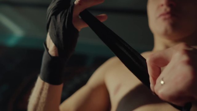 Male fighter is winding black elastic bandages on hands, close-up. He is preparing for training or boxing fight for protection