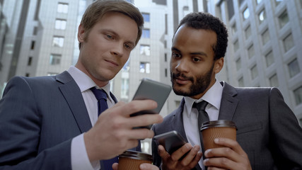 Multiracial colleagues reading news on smartphone at coffee break, office center