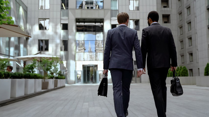 Two multiracial businessmen going to office building, discussing mutual work
