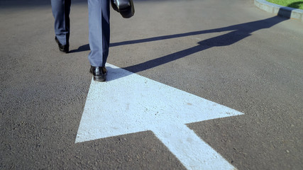 Young businessman walking along white arrow, choosing own way in life, concept
