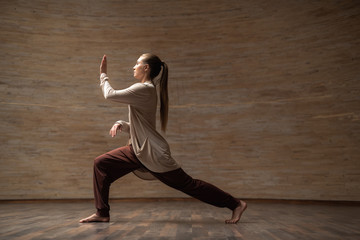 Calm long haired lady placing hands in front of her face and bending her knees while practicing chi...