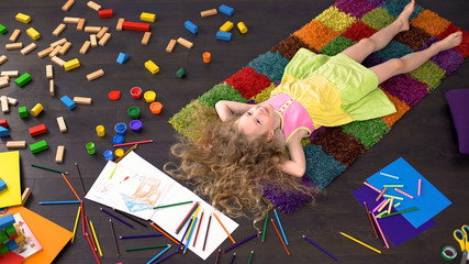 Adorable blond girl lying on carpet dreaming and smiling, happy childhood