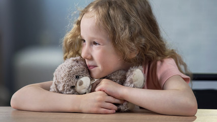 Little smiling girl hugging favorite teddy bear sitting at table happy childhood