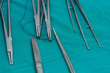 Needle holders with needles and sutures, surgical forceps and scissors on operating table