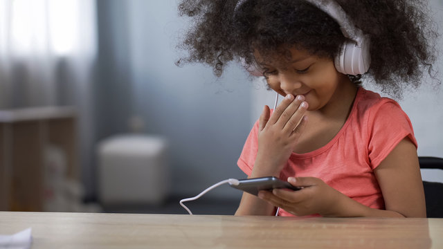 Little black girl smiling while surfing internet on smartphone, parental control