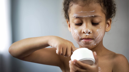 Adorable little girl holding tube with cream, copying mom behavior, cosmetics