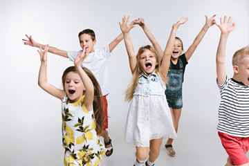 Obraz premium Group of fashion cute preschooler kids friends running together and looking at camera on a white studio background. The friendship, fashion, summer concept. Space for text.