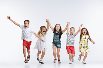 Obraz premium Group of fashion cute preschooler kids friends running together and looking at camera on a white studio background. The friendship, fashion, summer concept. Space for text.