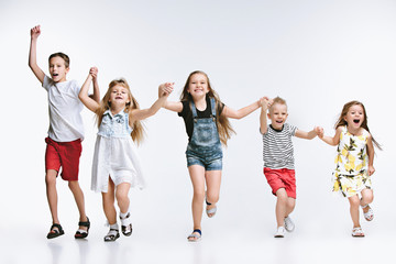 Obraz premium Group of fashion cute preschooler kids friends running together and looking at camera on a white studio background. The friendship, fashion, summer concept. Space for text.