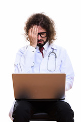 Studio shot of stressed man doctor using laptop while covering f