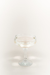 A glass of champagne with bubbles. Christmas balls and a golden lights on light abstract background.