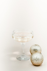 A glass of champagne with bubbles. Christmas balls and a golden lights on light abstract background.