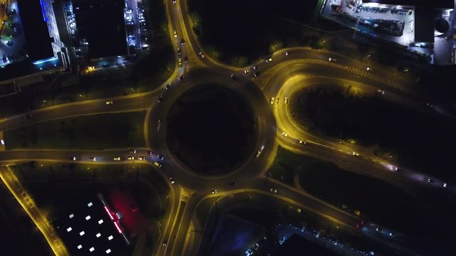 Roundabout night traffic aerial drone overhead view. Light traffic zoom out 
