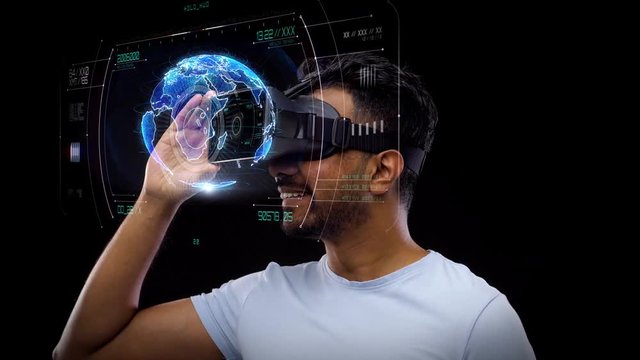 3d technology, future and people concept - young indian man in vr glasses or virtual reality headset with earth projection over black background