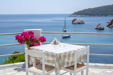 Restaurant tables waiting for customers by the sea outdoor terrace in Skopelos, Greece.