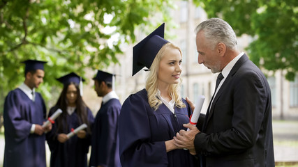 Excited dad congratulating graduate daughter in park near academy, happiness