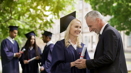 Happy father congratulating graduate daughter holding her hands near university