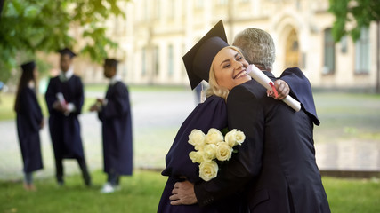 Father hugging his graduate daughter giving flowers, congratulating, paternity