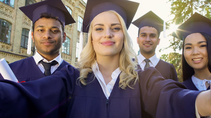 Students in academic regalia taking selfie on graduation day, achievement
