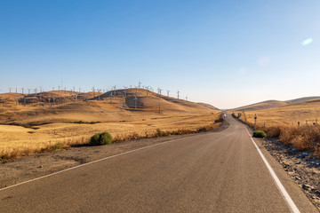 Fototapeta na wymiar A road through the Californian countryside with a wind farm on the hills around