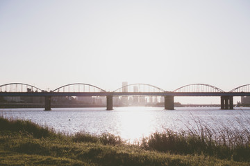 Fototapeta na wymiar a calm river and an arch bridge and green grass and blue sky