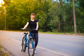young beautiful girl leads the bike on the sidewalk