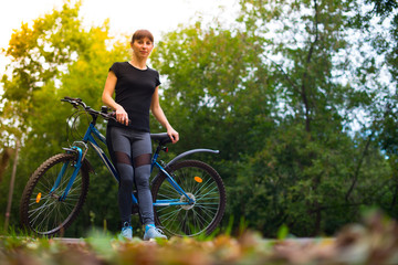 Naklejka premium Young beautiful athletic girl in sportswear sitting on a blue bike frame. Trees on the background.