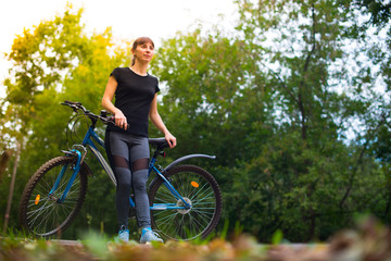 Young beautiful athletic girl in sportswear sitting on a blue bike frame. Trees on the background.