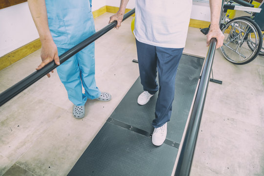 Disabled senior helped by the physiotherapist is doing rehabilitation on the footboard