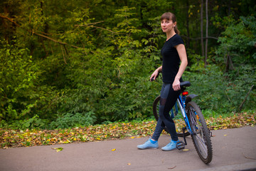 Young beautiful athletic girl in sportswear sitting on a blue bike frame. Trees on the background.