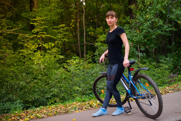 Obraz premium Young beautiful athletic girl in sportswear sitting on a blue bike frame. Trees on the background.