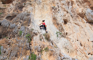 A young woman with a rope engaged in the sports of rock climbing on the rock.