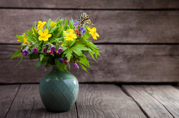 butterfly and bouquet of field wild flowers in a vase on old boards.