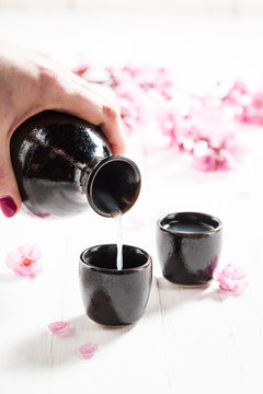 Pouring sake to dark ceramics and blooming flowers on table