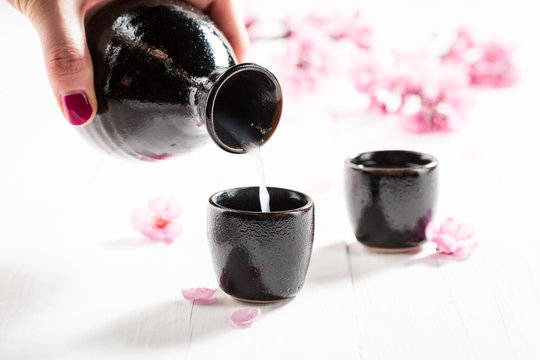 Pouring strong sake into dark ceramics on white table