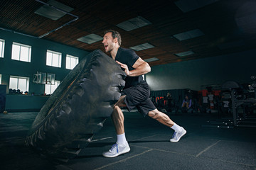 Fototapeta premium Shirtless young fit man flipping heavy tire at gym. The exercise, fitness, sport, workout, athlete, power, training, bodybuilding concept