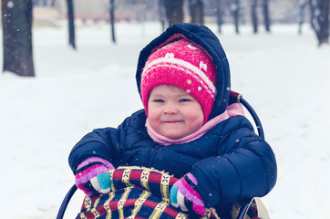 Little girl sitting on her sled in winter day.