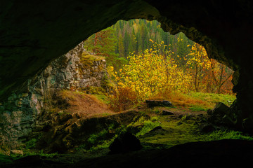 view from the dark natural cave to the bright autumn mountain landscape outside