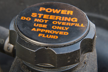 Closeup of a cap of a power steering oil tank. Do not overfill and use approved fluid only warning text. - obrazy, fototapety, plakaty