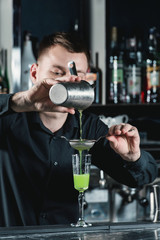 Fototapeta na wymiar bartender making Green Alcoholic Cocktail pouring fluid into glass.