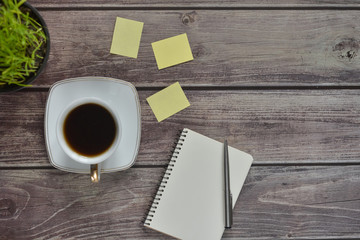 Wooden office desk table with a notebook, a handle, a cup of coffee and a flower pot. Top view with copy space.