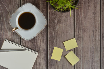 Wooden office desk table with a notebook, a handle, a cup of coffee and a flower pot. Top view with copy space.