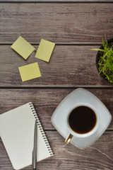 Wooden office desk table with a notebook, a handle, a cup of coffee and a flower pot. Top view with copy space.
